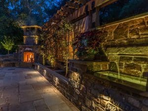 A stone patio with a fire pit and lighting at night.