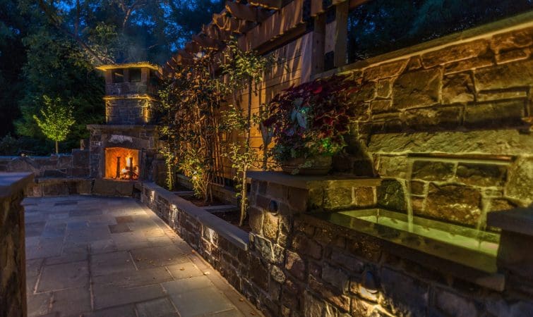 An outdoor stone patio with a fire pit and ambient lighting at night.