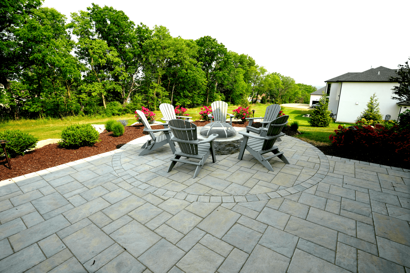 A picturesque landscape design featuring a patio adorned with comfortable chairs surrounding a mesmerizing fire pit.