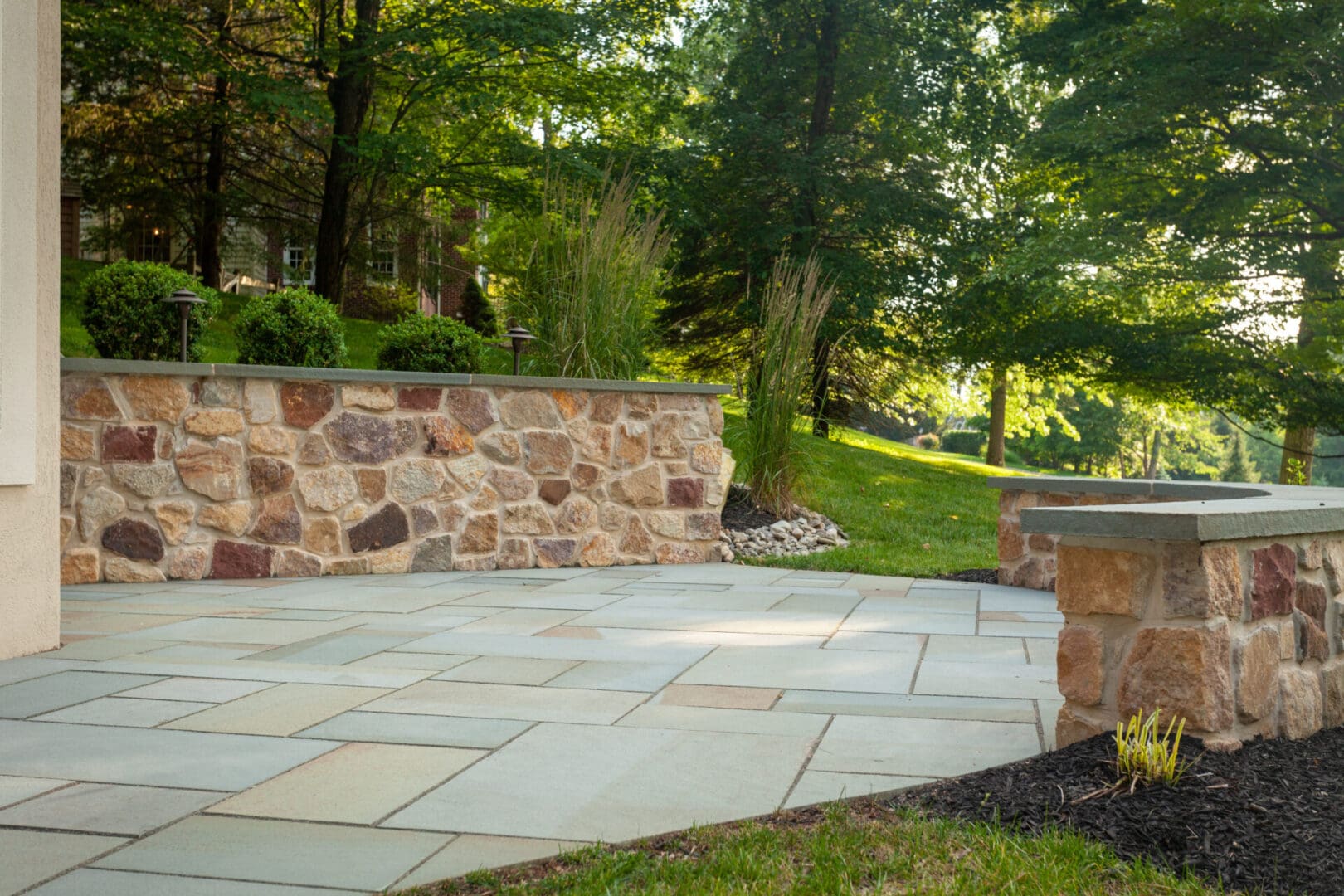 A stone patio with a stone wall and a stone bench, designed with landscape design principles.