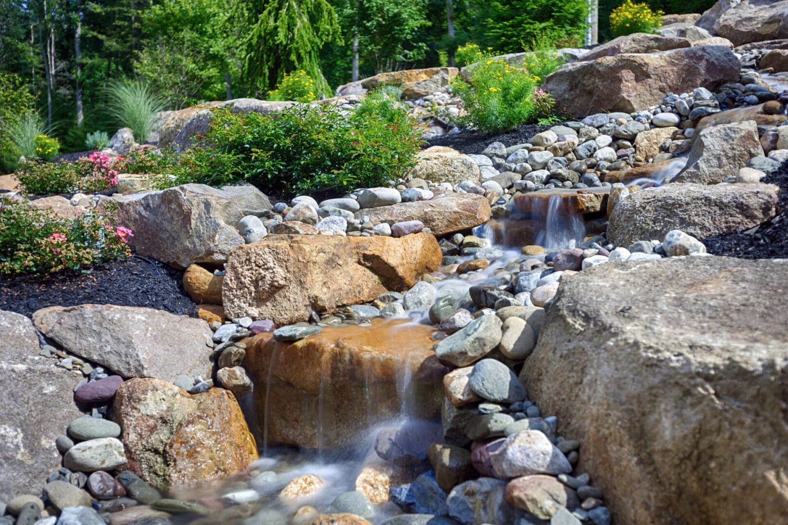 A garden with a waterfall, rocks, and flowers, highlighting its serene water features.
