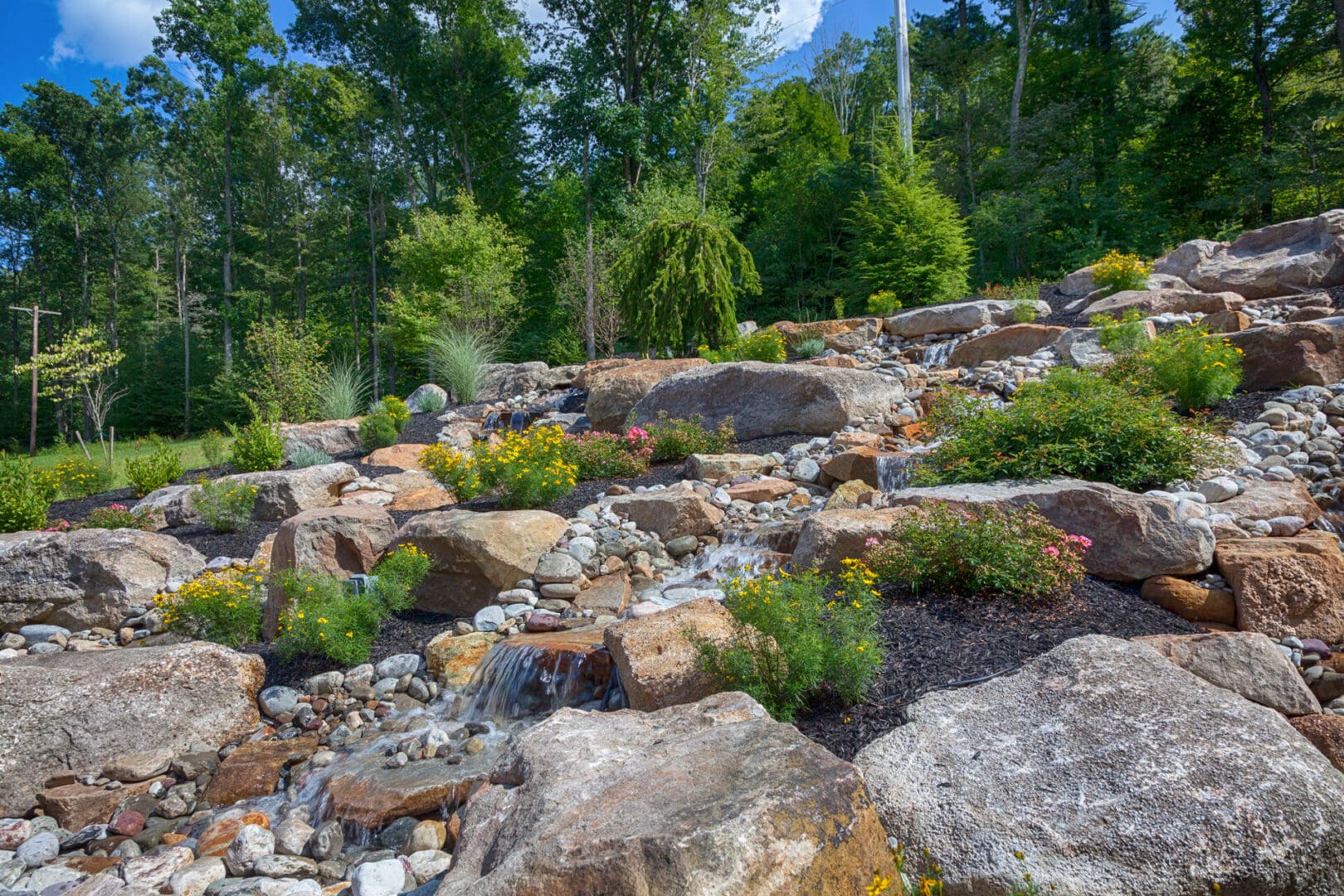A serene rock garden surrounded by trees and shrubs, enhanced with subtle water features