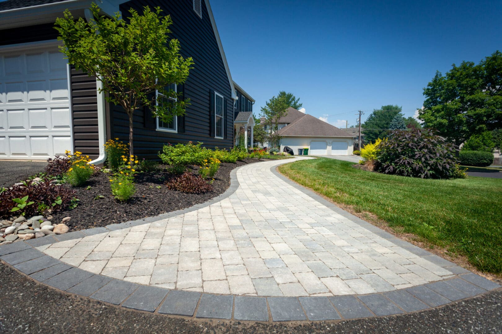 A driveway with brick pavers in front of a house, showcasing landscape design.
