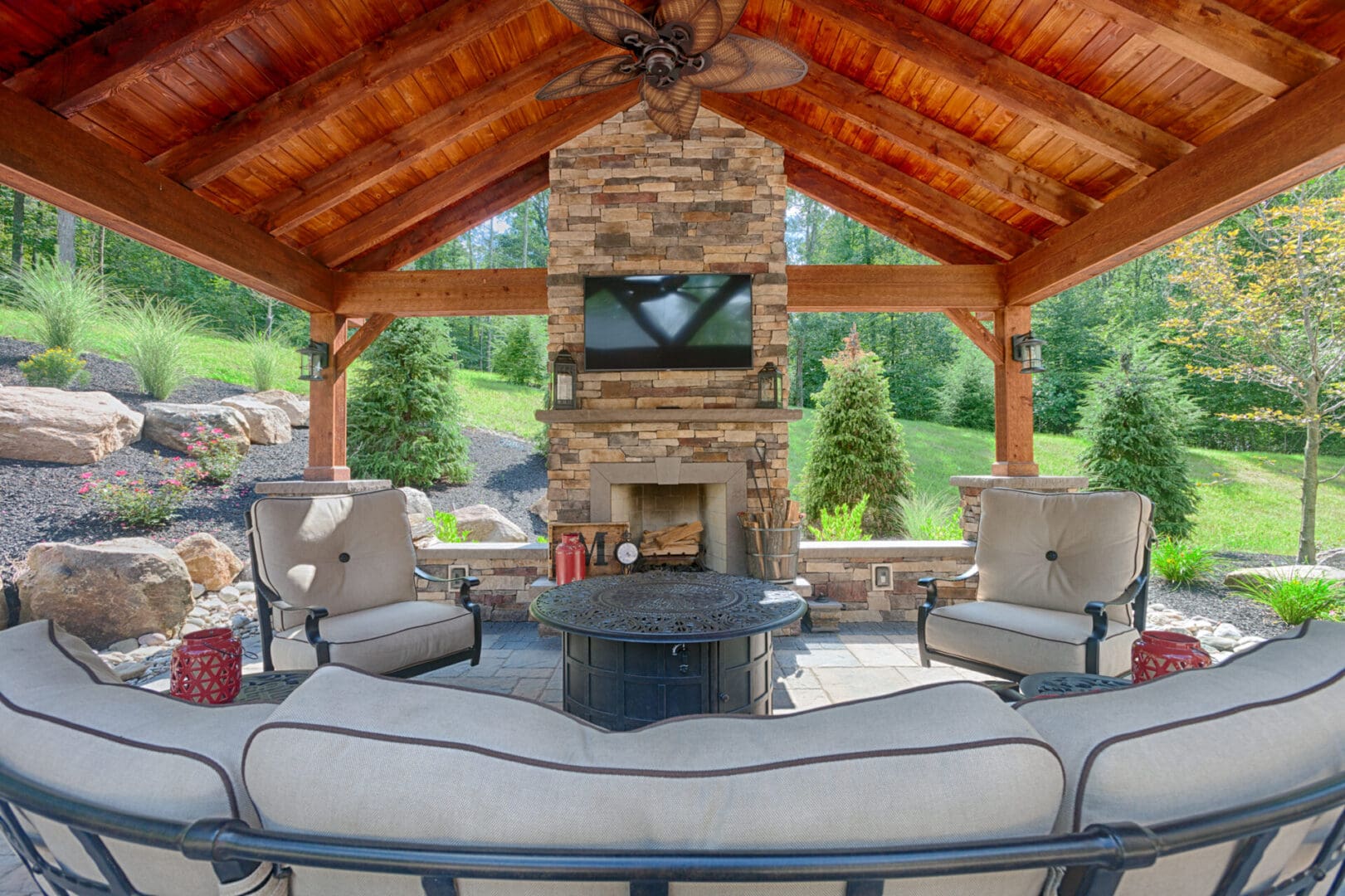 A stone covered patio with a custom fireplace and TV.