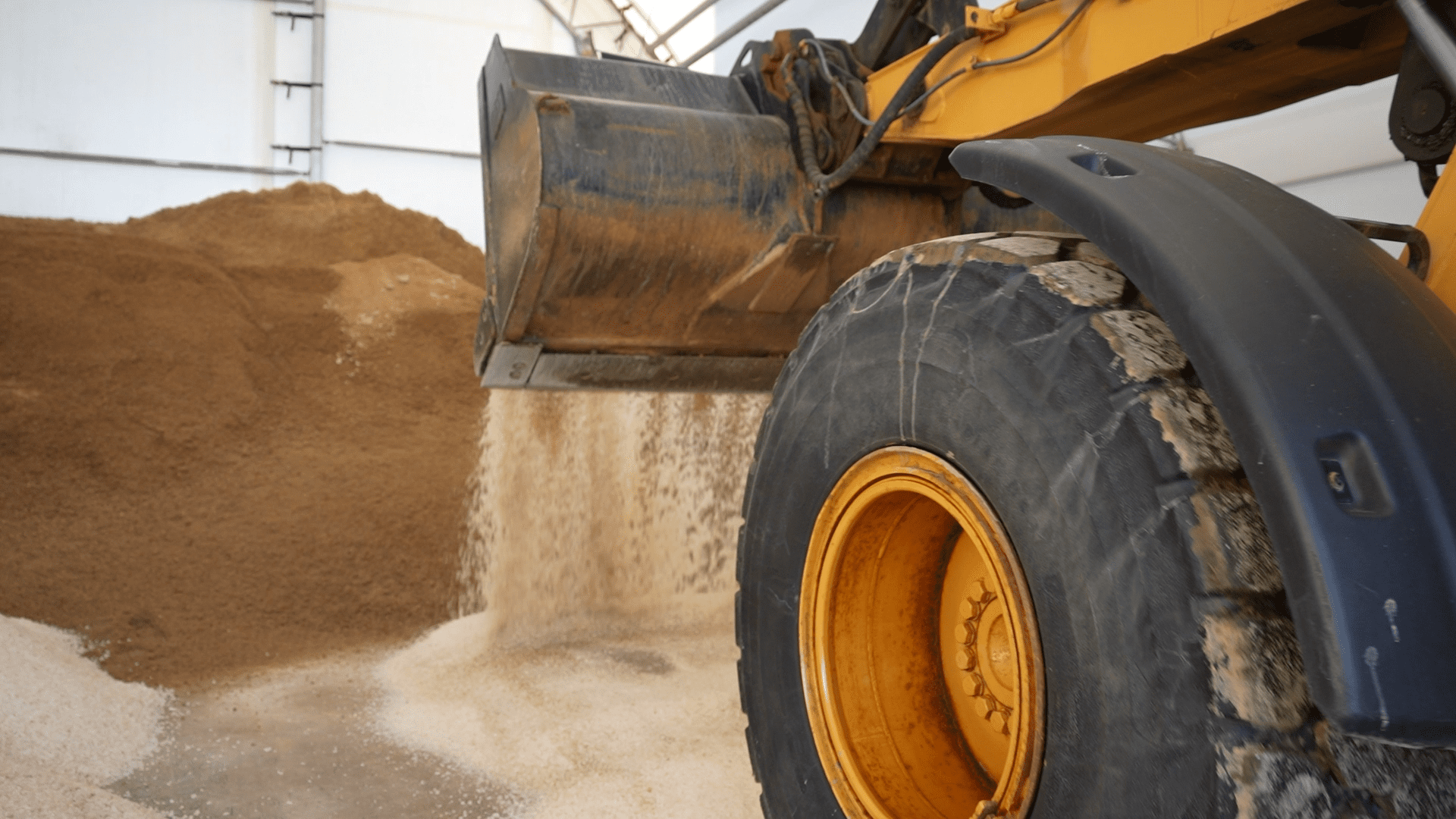 A commercial bulldozer is loading sand into a silo for snow and ice management purposes.