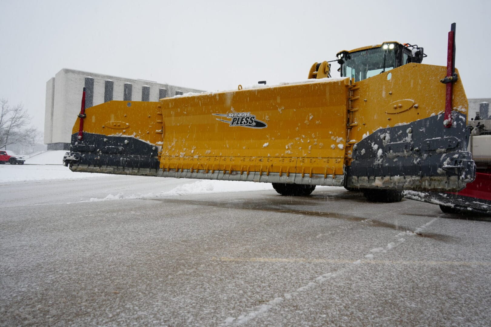 A commercial yellow snow plow is driving down a snowy road.