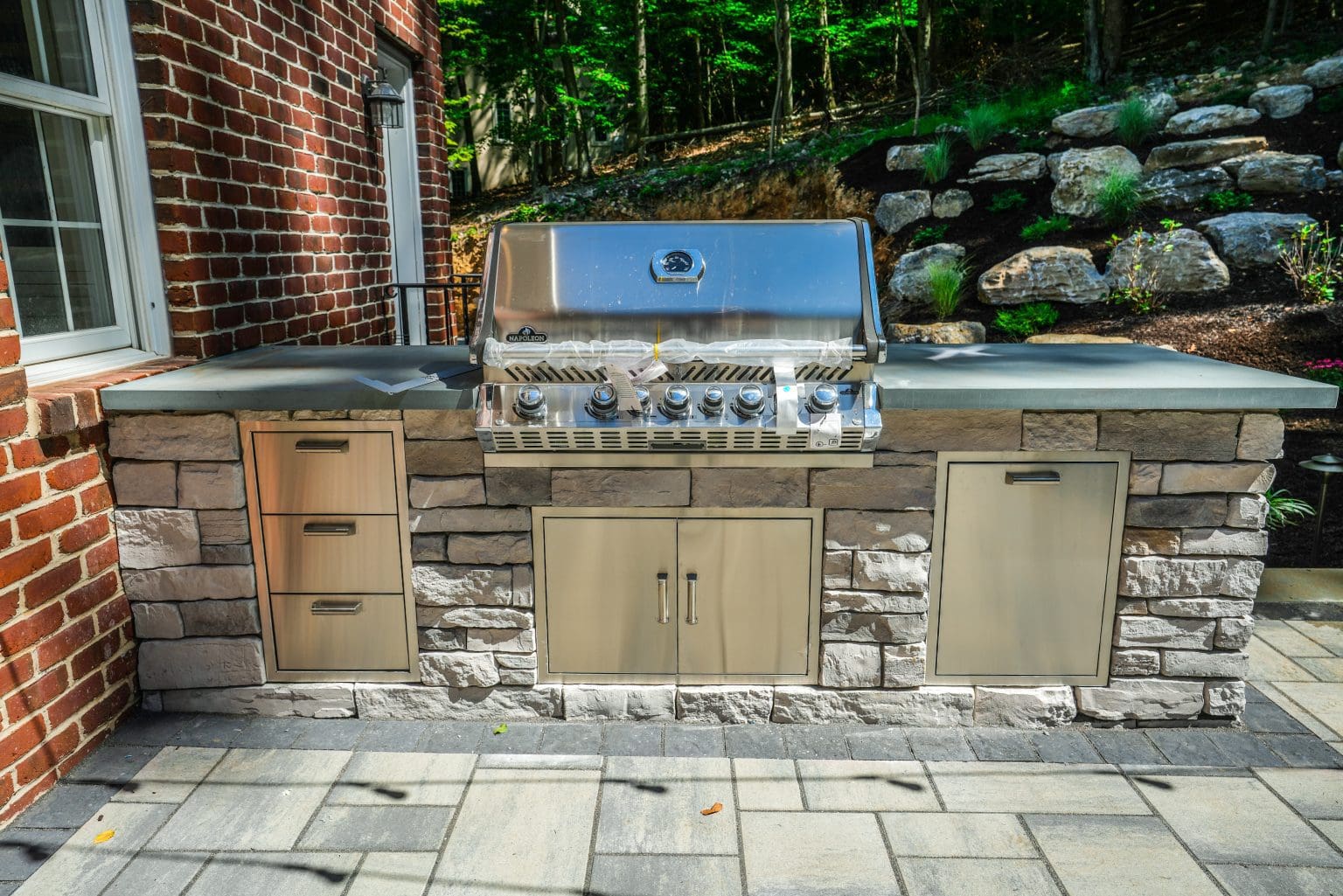 A landscape design featuring an outdoor kitchen with a grill and sink.