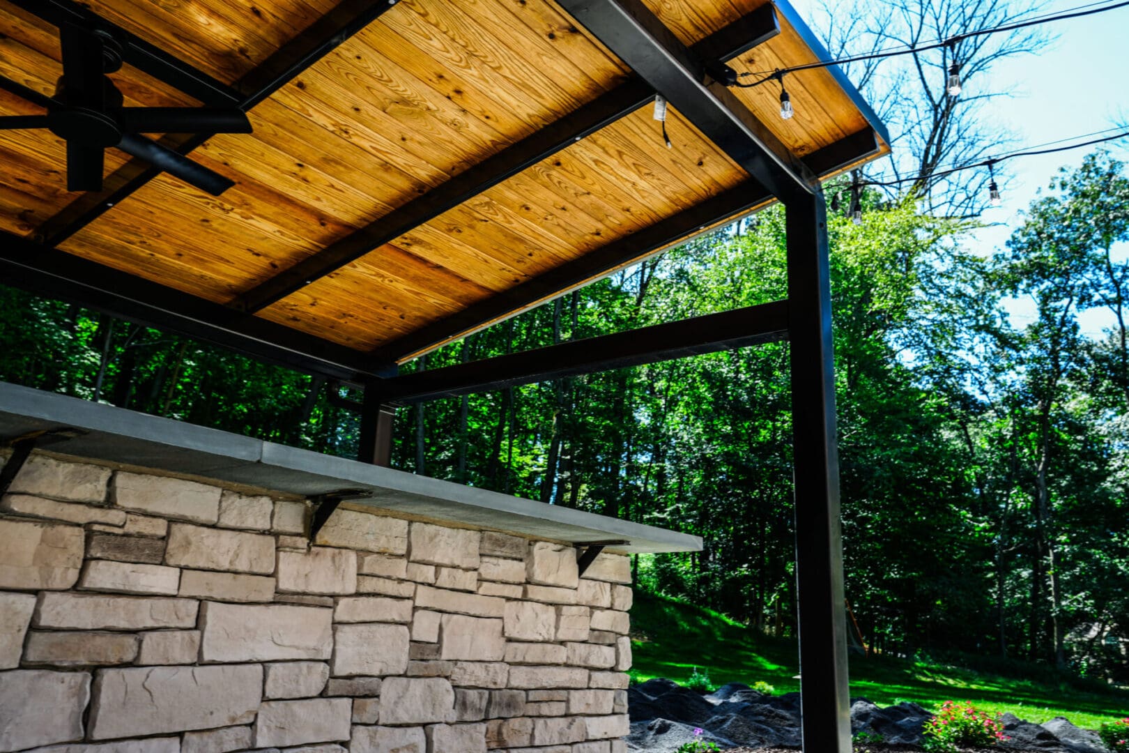 A custom outdoor patio with a stone wall and a ceiling fan.