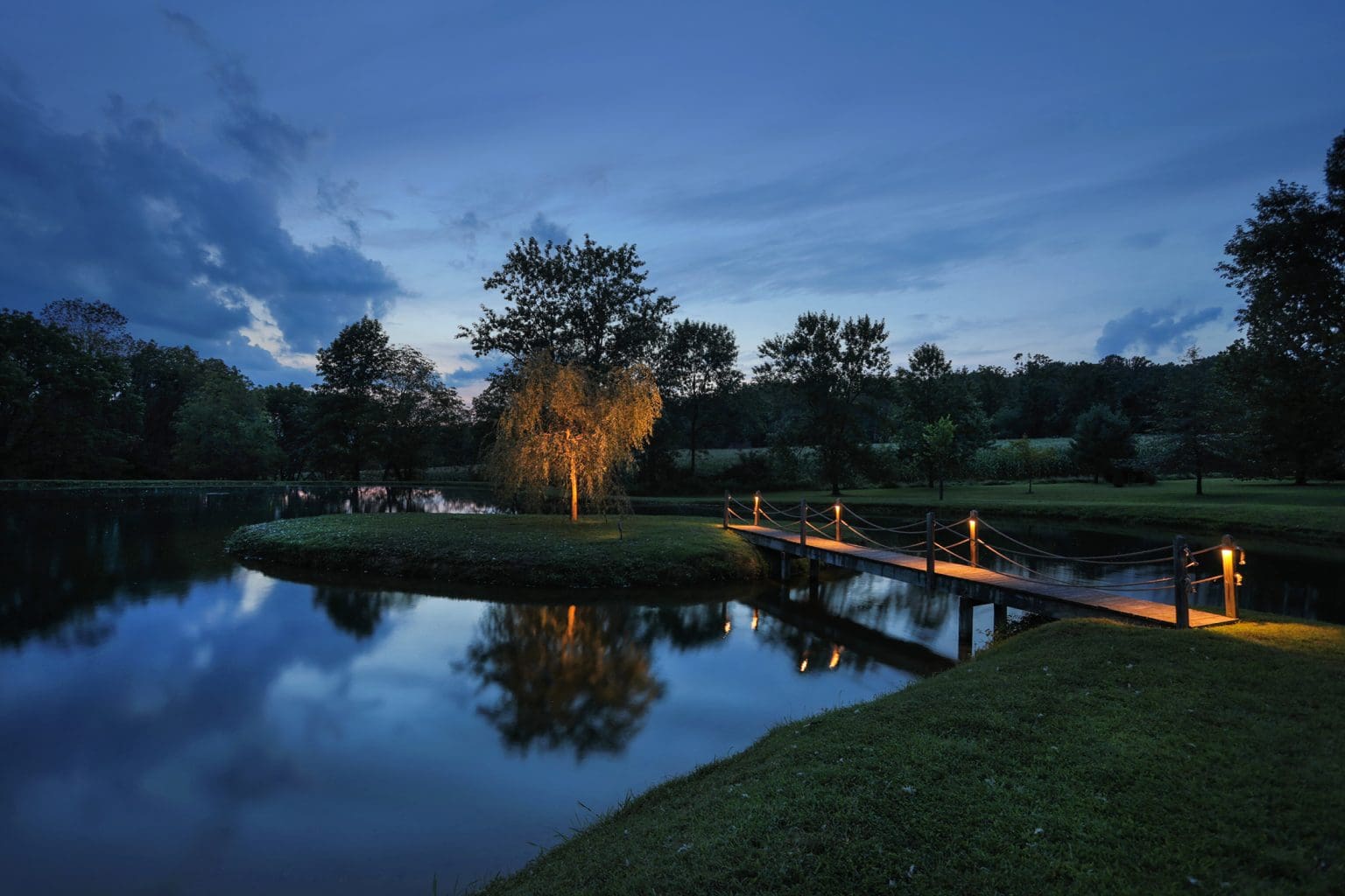 A serene landscape design featuring a wooden bridge over a peaceful pond during the enchanting hours of dusk.