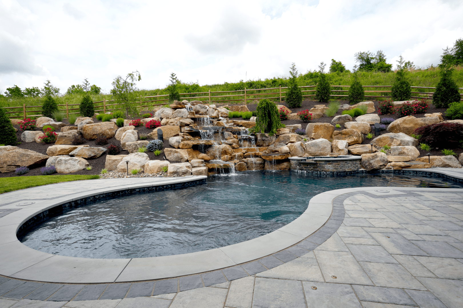 A pool with a waterfall and rocks surrounded by Planting Professionals.
