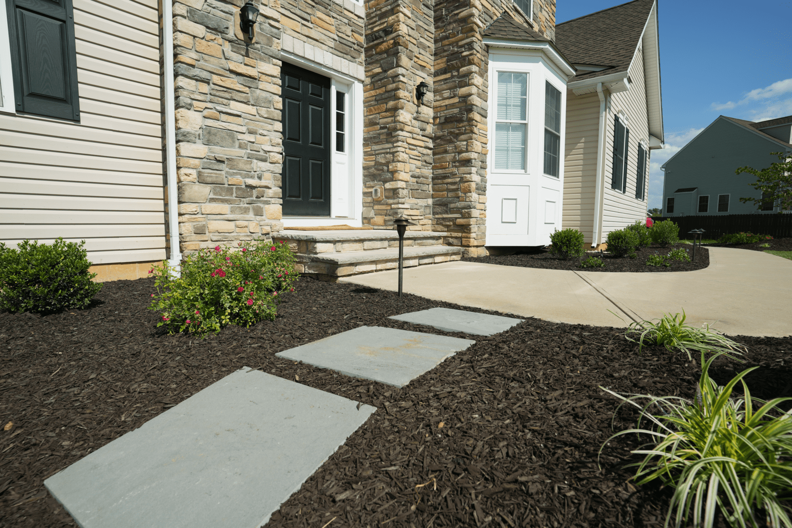 A stone walkway leading to a house, professionally designed by planting professionals.