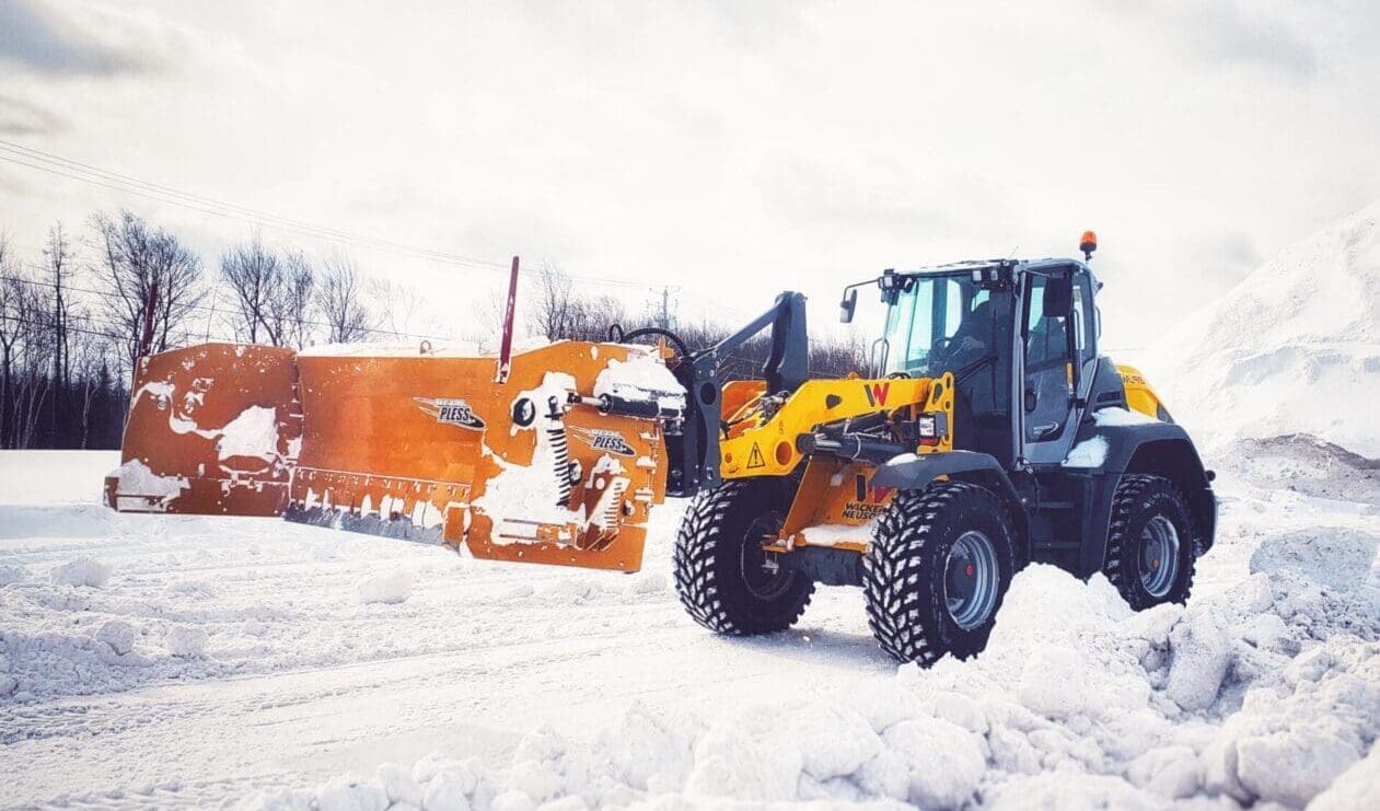 A metal pless bulldozer is parked on a snowy field.