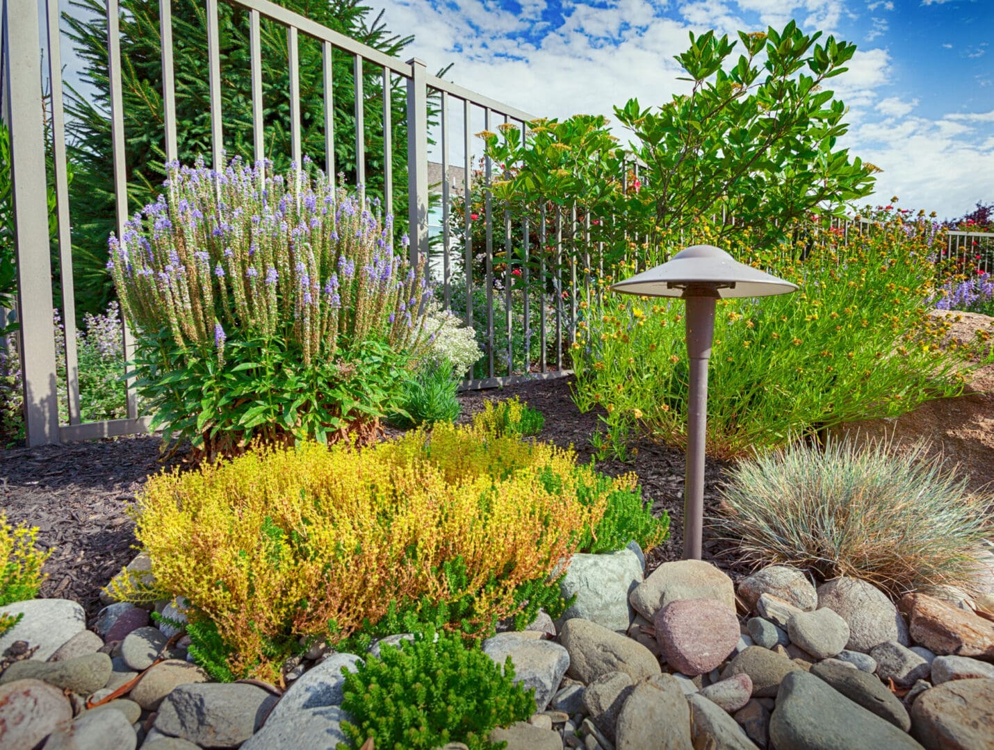 A garden with a fence and rocks, enhanced by outdoor lighting.