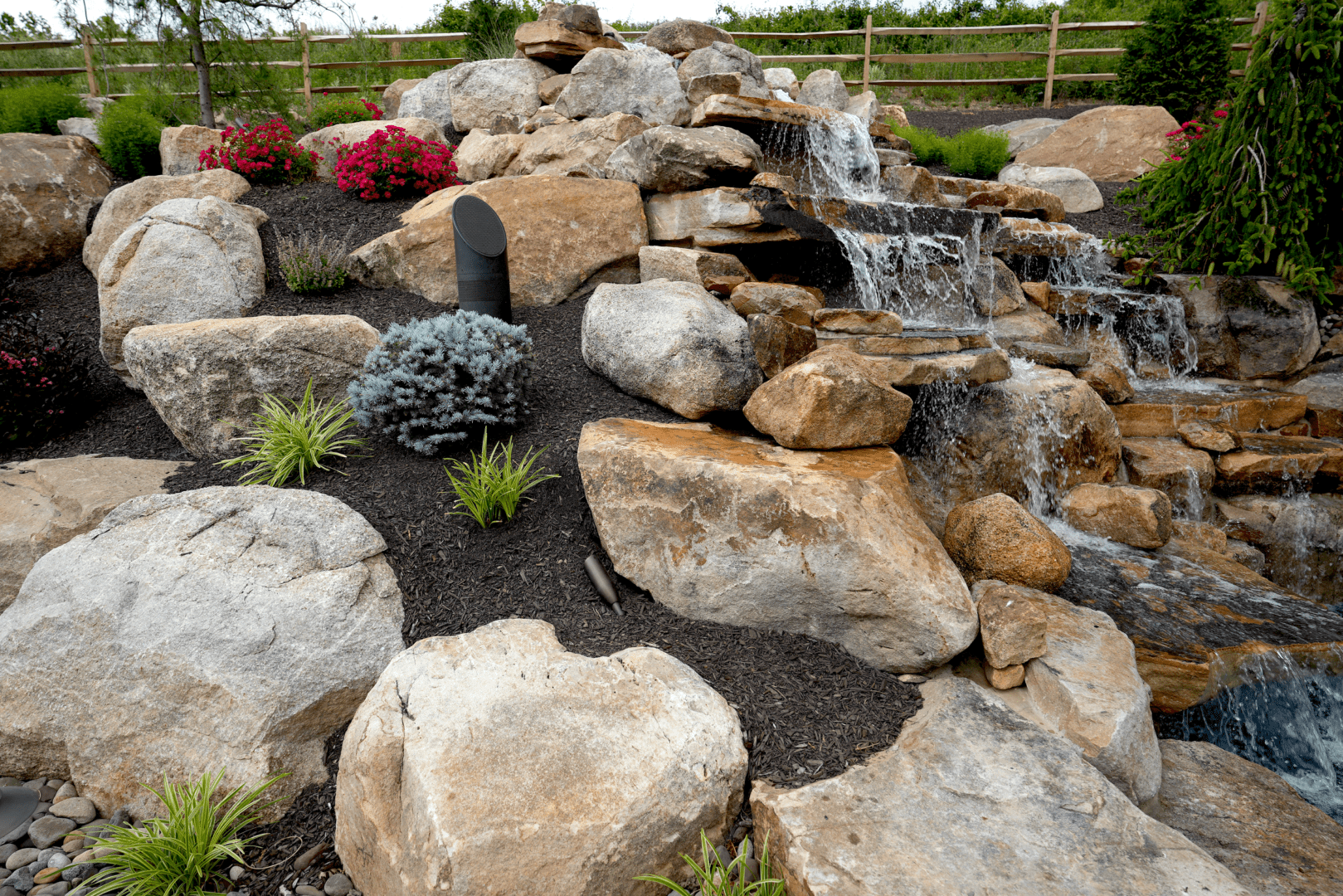 A garden with rocks, outdoor lighting, and a waterfall.