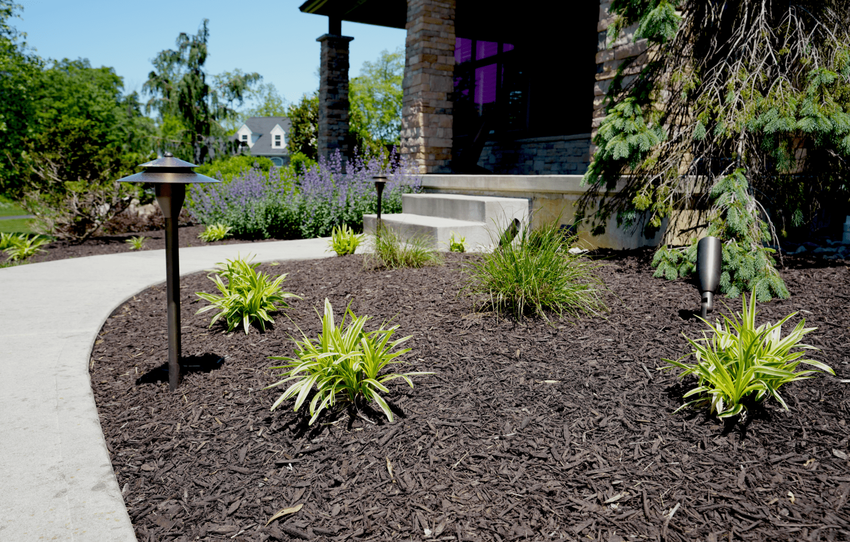 A brown mulch in front of a house with outdoor lighting.