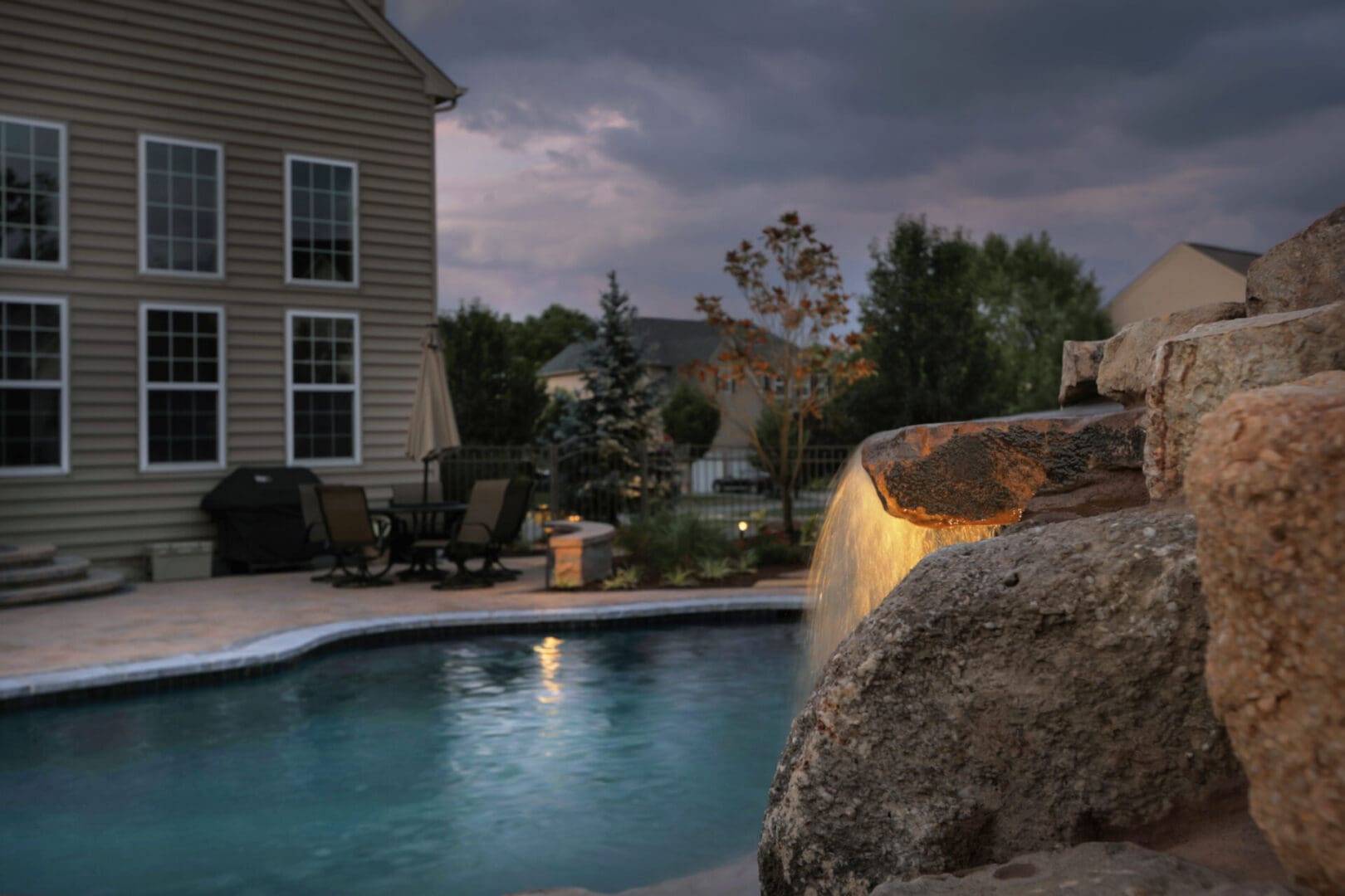A pool with a waterfall and outdoor lighting in the background.