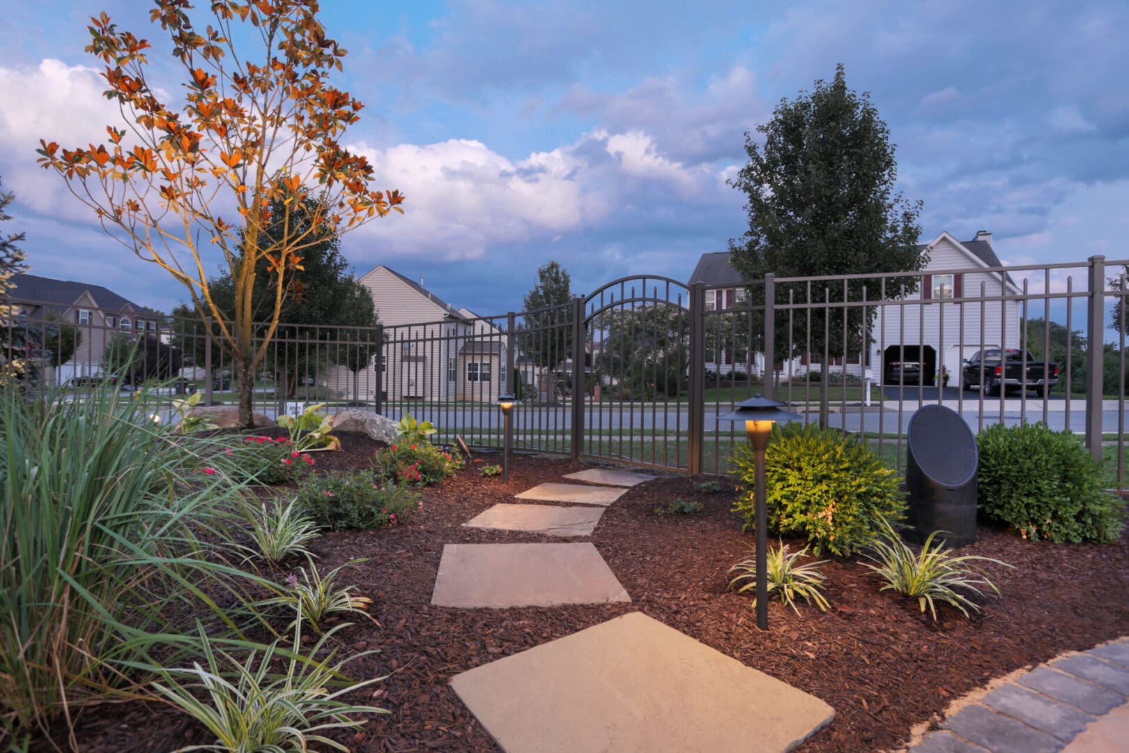 A pathway illuminated with outdoor lighting, leading to a serene garden in a residential neighborhood.
