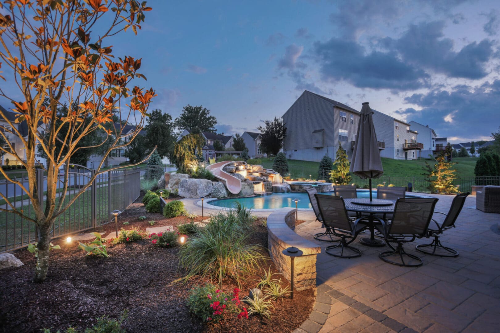 A backyard with outdoor lighting and a pool at dusk.