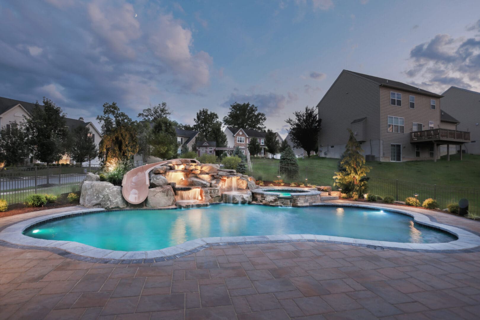 A backyard pool with a waterfall and outdoor lighting.