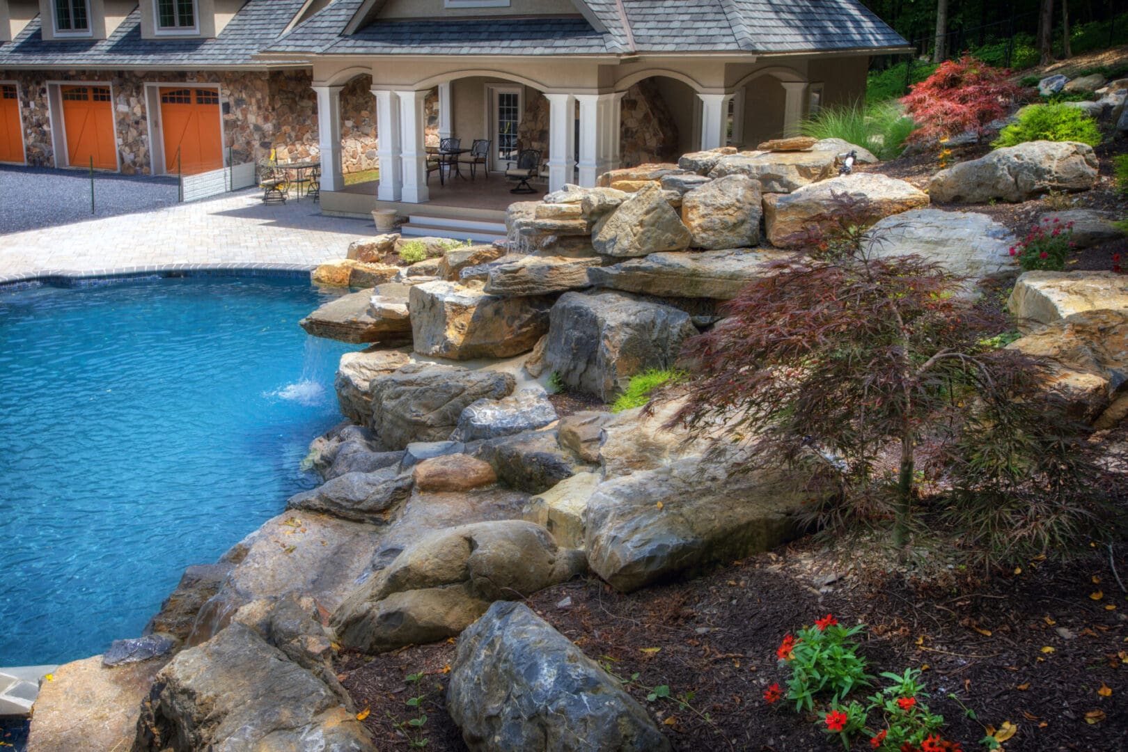 A backyard with a pool and landscaping featuring boulders.