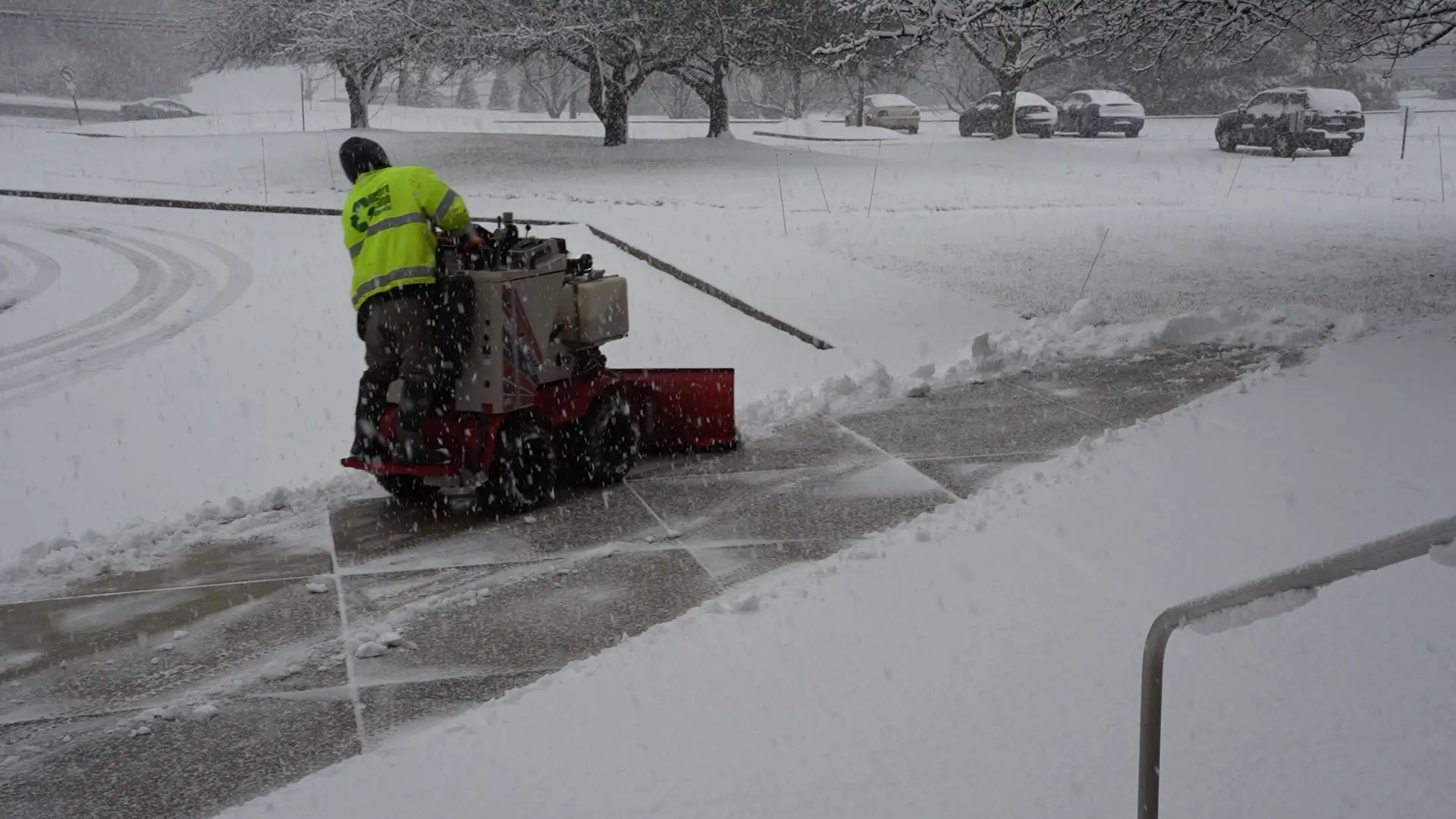 A man providing commercial snow and ice management services with a snow blower on a sidewalk.
