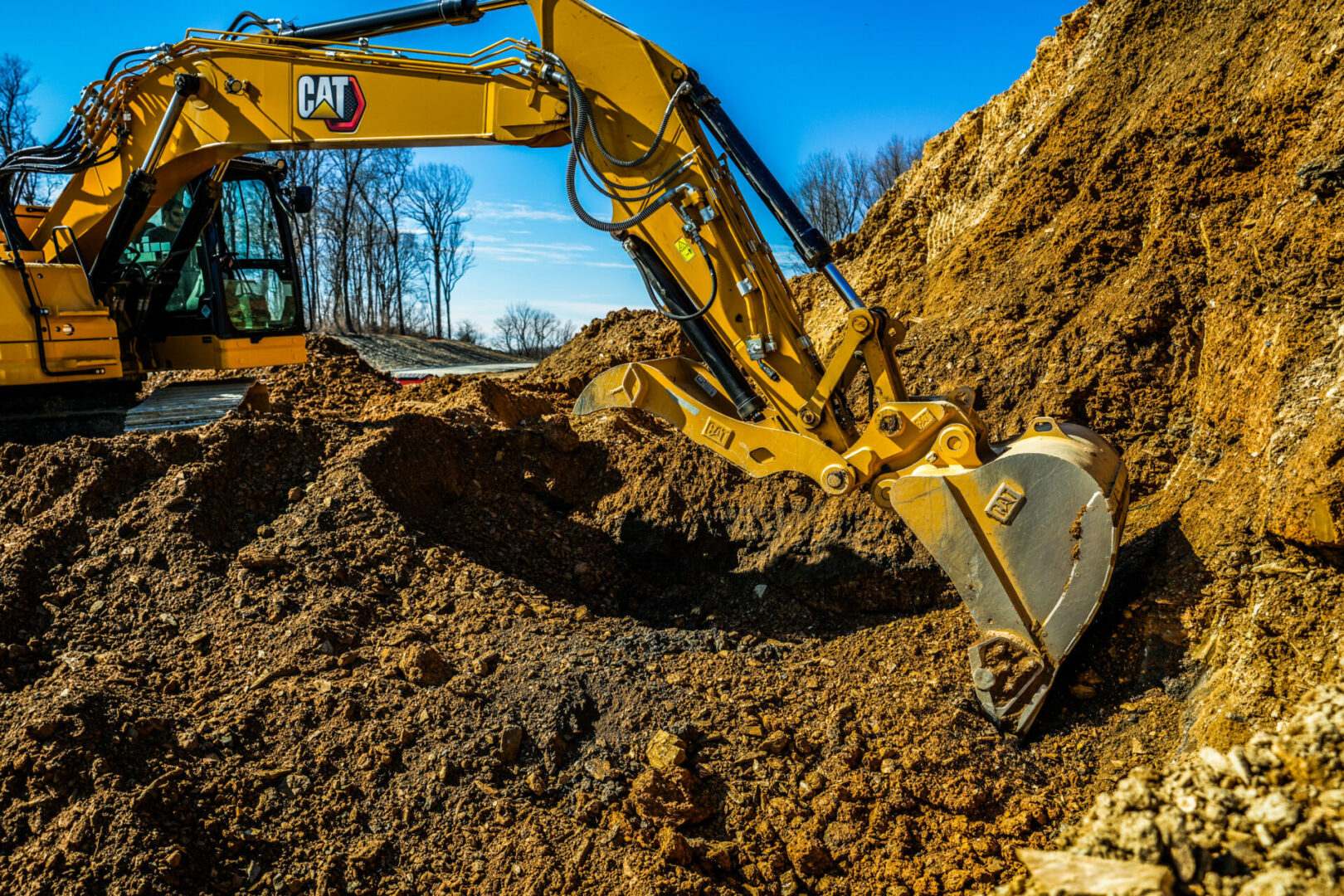 A caterpillar excavator is performing site work, digging into a pile of dirt.