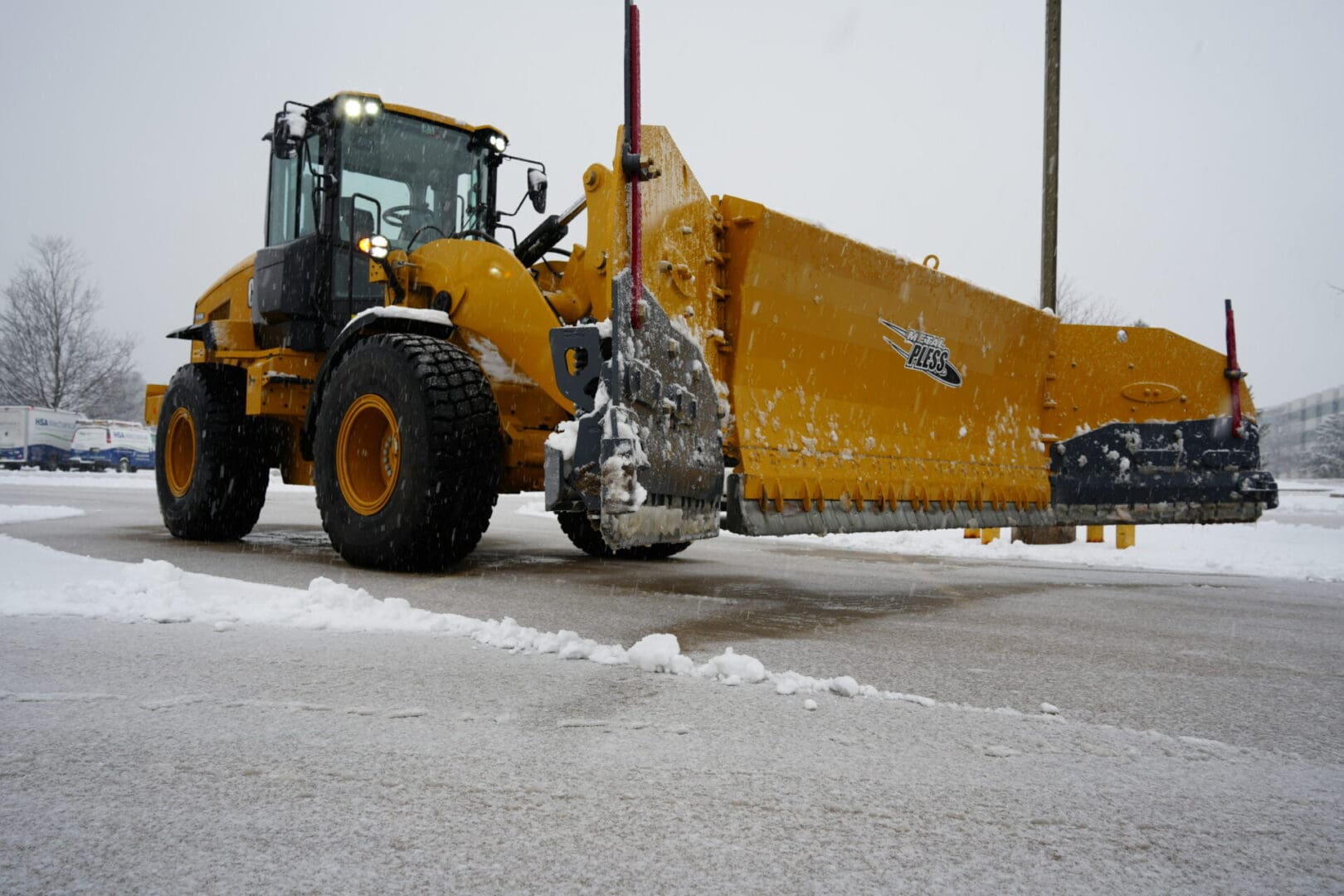 A yellow tractor with snow plow attachment on the side of road.