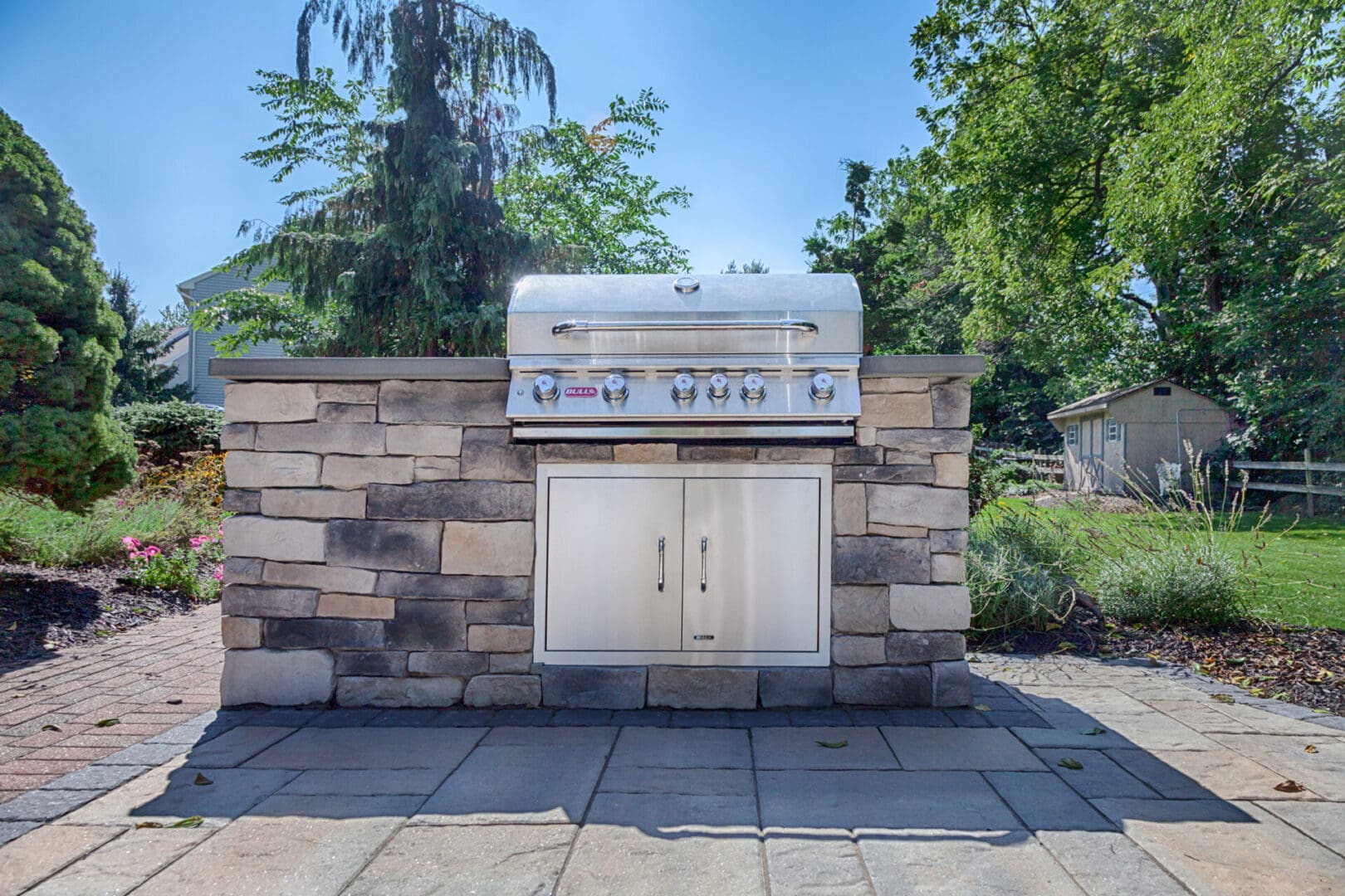 A custom outdoor kitchen featuring a bbq grill on a stone wall in a backyard.