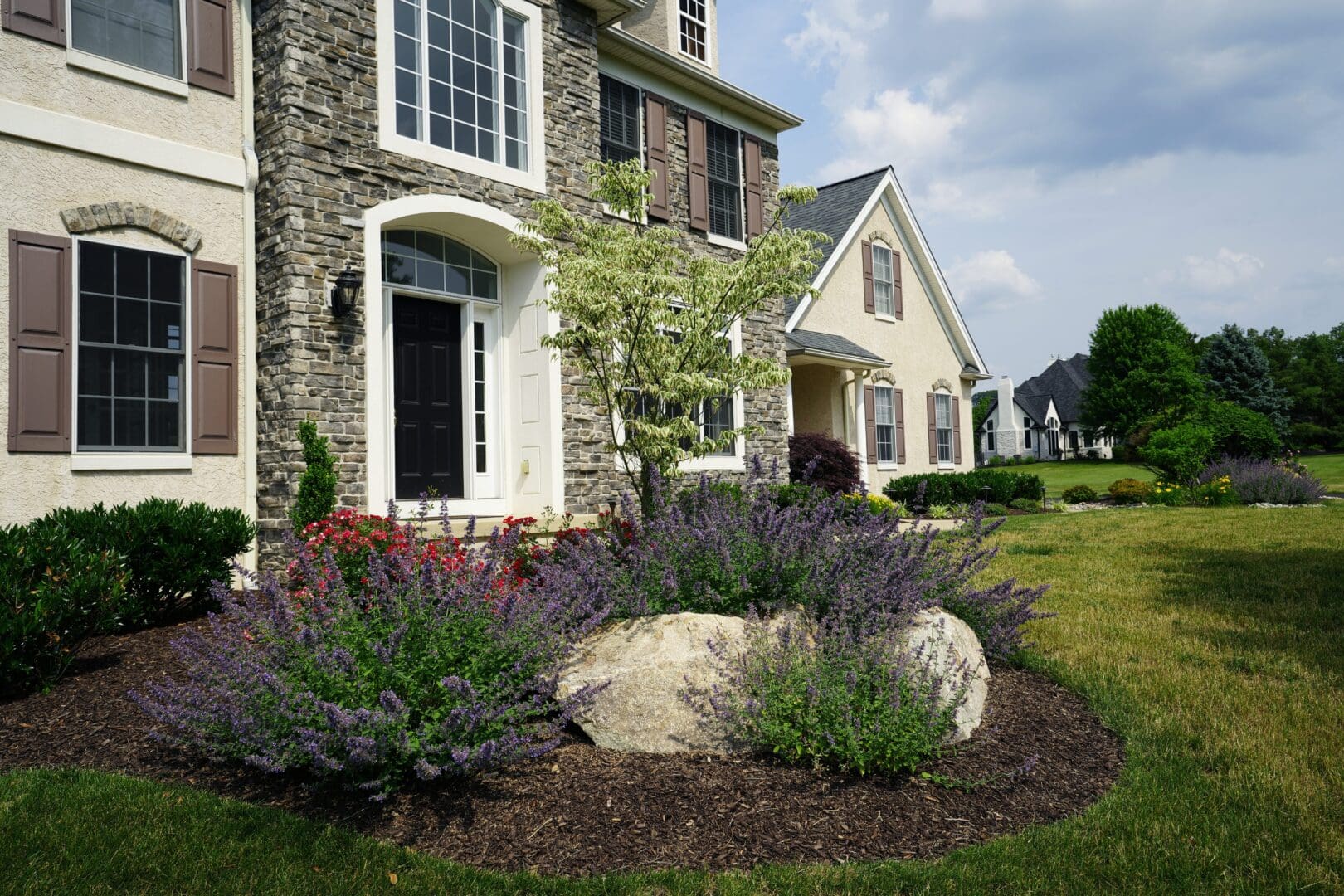 A large rock in front of a house with purple flowers.