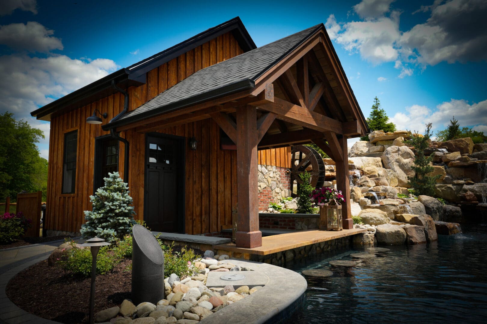 A wooden house with a pond and rocks in front of it.