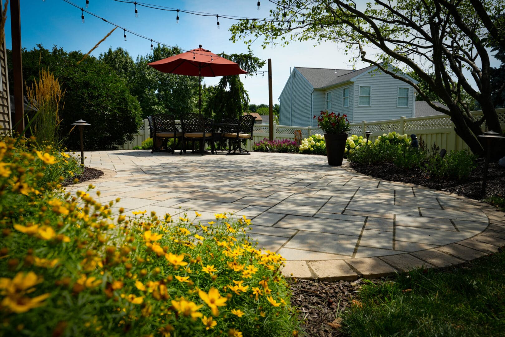 A patio with an umbrella and flowers in the background.