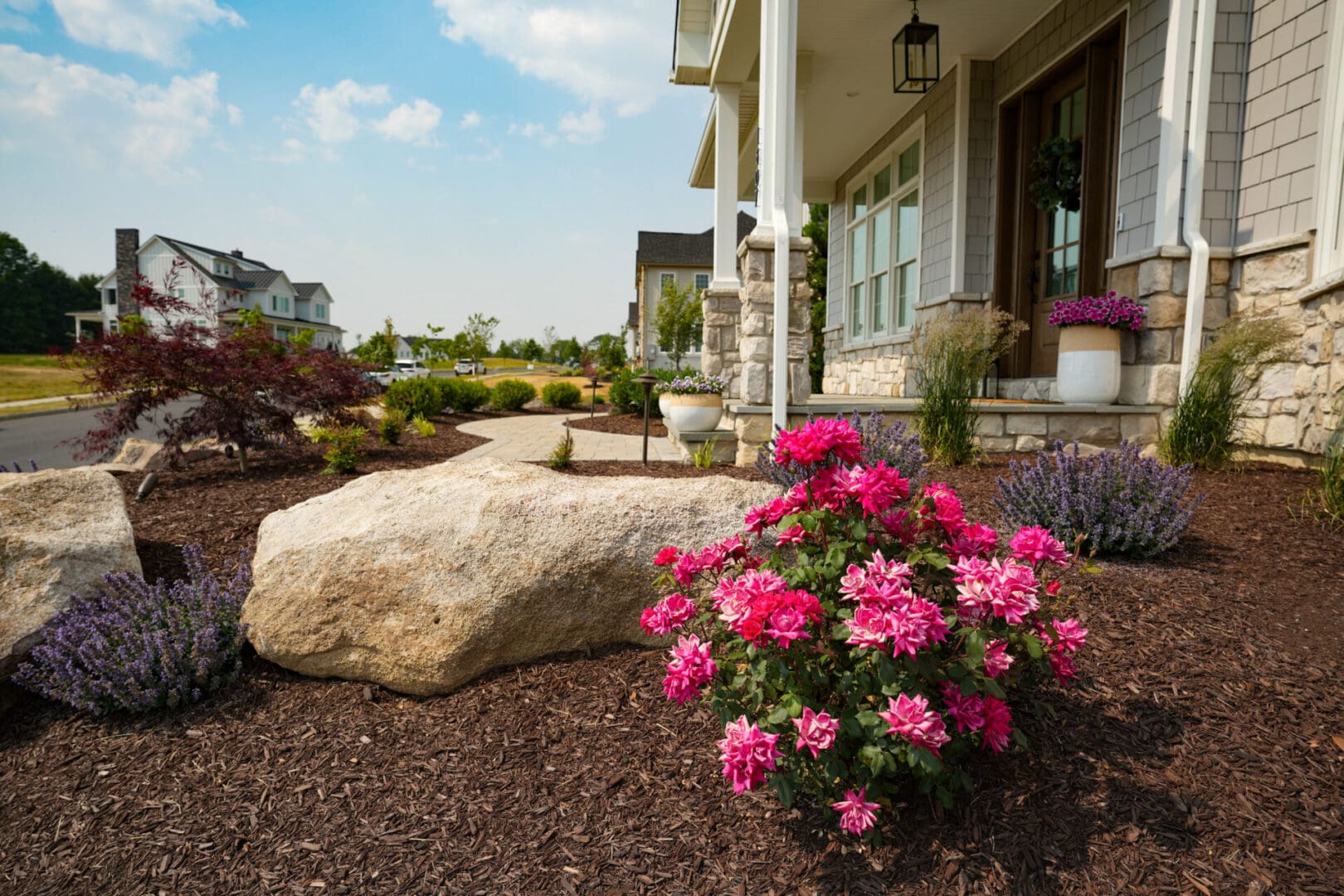 A large rock in front of a house with flowers growing.